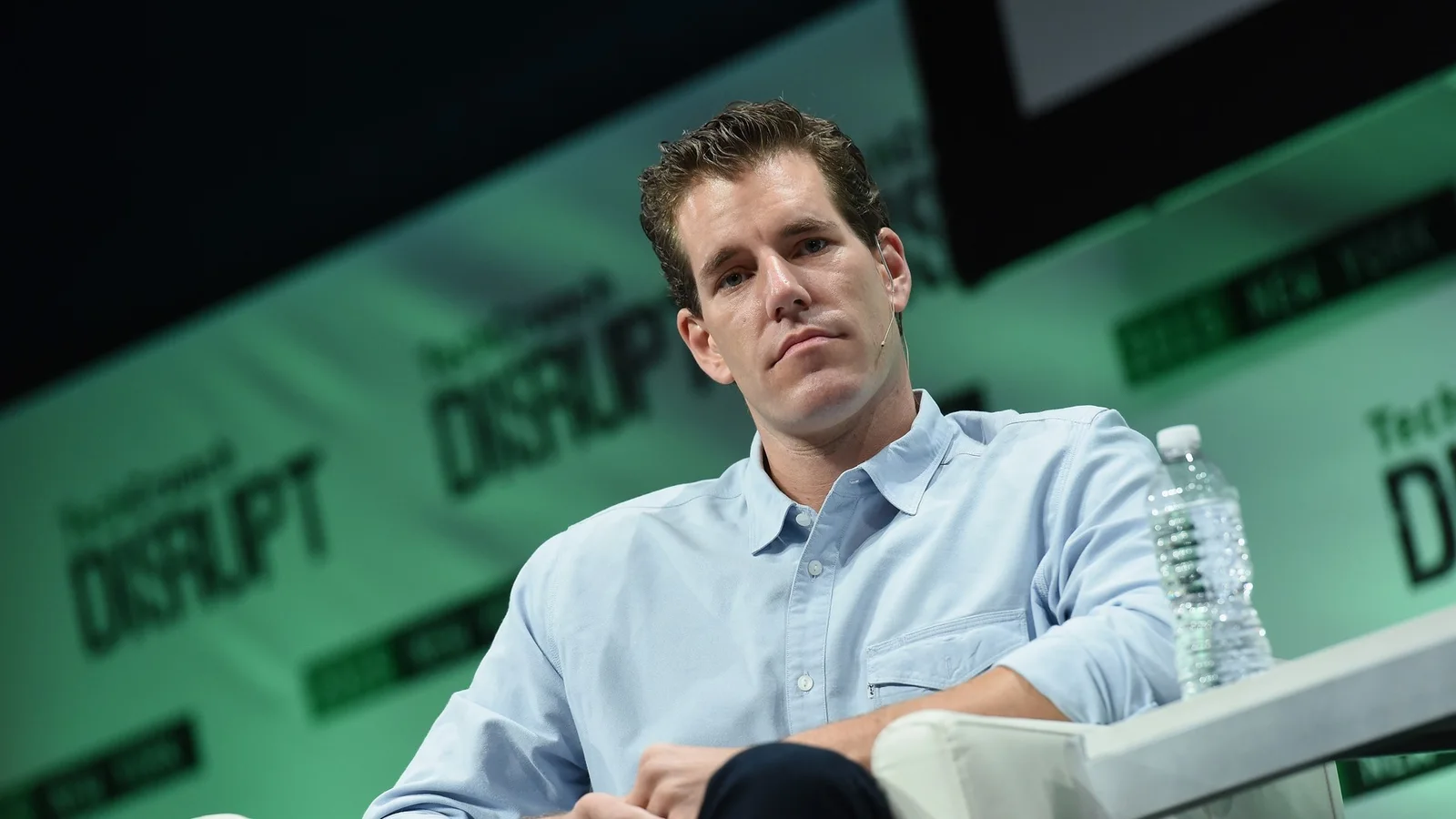 Cameron Winklevoss, co-founder of Winklevoss Capital, sits onstage in a light blue button-down shirt at TechCrunch Disrupt NY 2015, wearing a headset microphone.