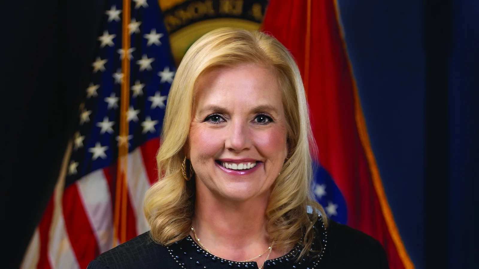 Catherine Hanaway, Missouri attorney general, in an official portrait, smiling in a dark jacket in front of the U.S. and Missouri flags
