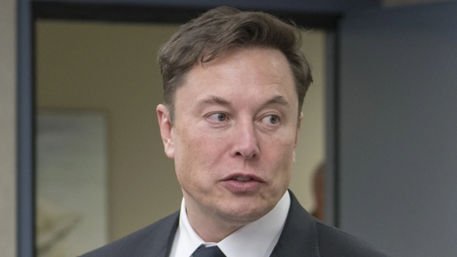 Elon Musk, CEO of SpaceX, in a dark suit and tie, looking to his left while holding a small model of the Starship rocket during a 2019 visit to military leaders in Colorado Springs