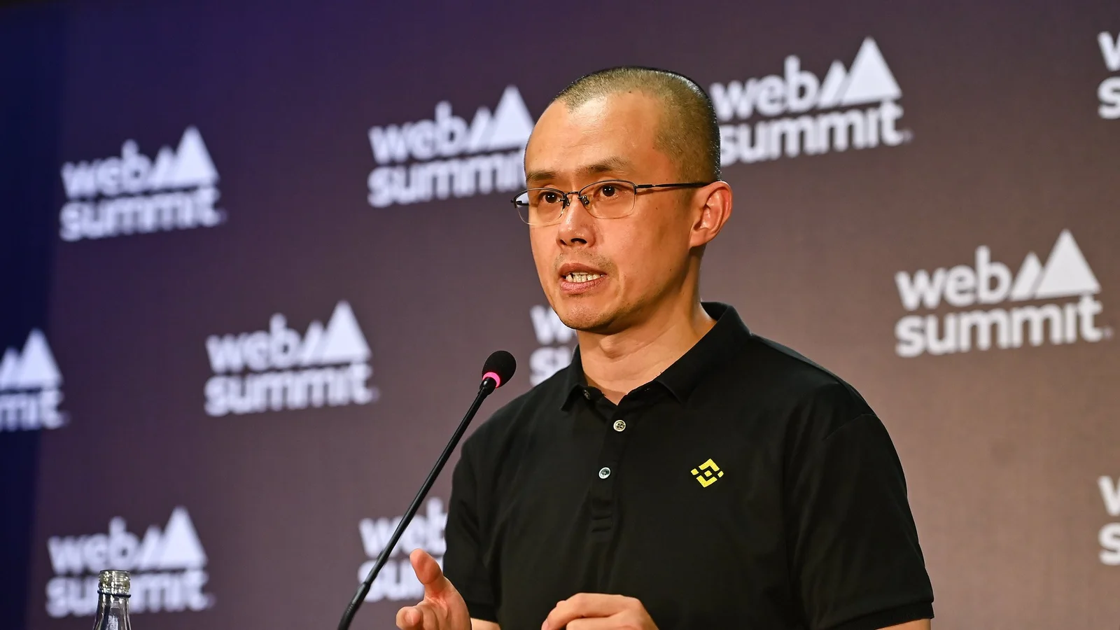 Changpeng Zhao, Binance co-founder and CEO, in a black Binance polo speaking into a microphone and gesturing at a Web Summit 2022 press conference in Lisbon